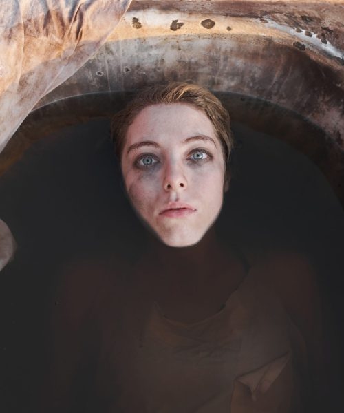 High angle view of young sad woman with dirty face lying in the bath with dirty water outdoors and looking up